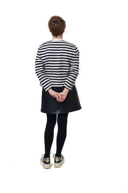 Back view full length portrait of a woman in skirt striped sweater and sneakers with hands on back on white background