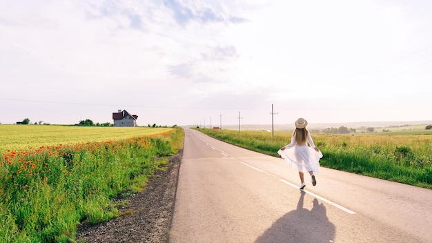 Back view of girl in dress and boater walks on the road near the