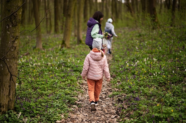 Back view of girl and mother walking on forest trail Outdoor spring leisure concept