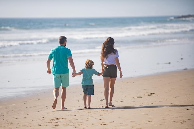 Back view of happy family on the beach People having fun on summer vacation Father mother and child holding hands against blue sea Holiday travel concept