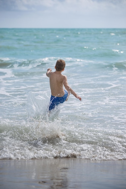 Back view on happy kid boy running into ocean or sea waves for swimming Happy summer vacations