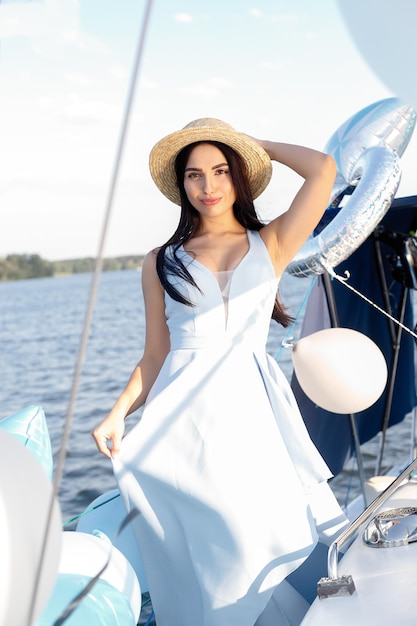 Back view of joyful attractive amazing woman in blue dress and hat enjoying azure water on the deck of a sailing yacht Concept of sailing regatta luxury vacation at sea