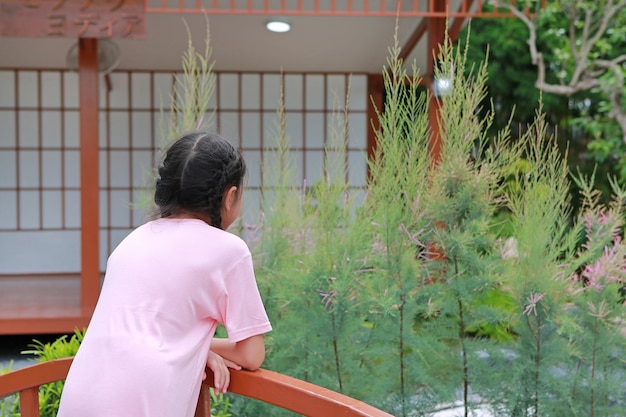 Back view little Asian child girl standing on bridge and looking something in the garden