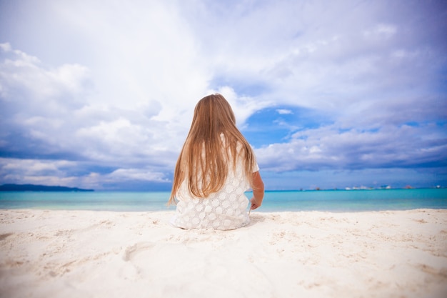 Back view of little cute girl siiting on the beach