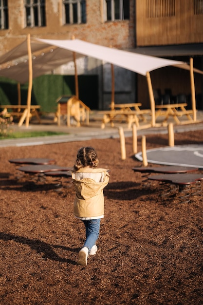 Back view of little girl walking in little kids city toy city for children outdoors road of sawdust