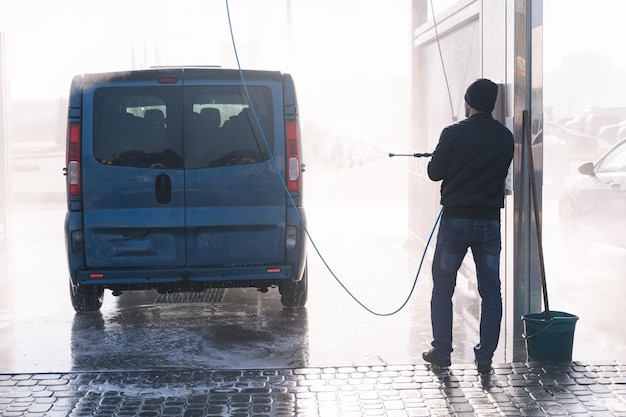 Back view of man cleaning his car with a jet sprayer self service car washing