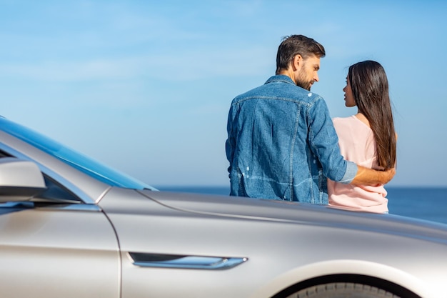 Back view of man embracing woman and looking at each other leaning the car