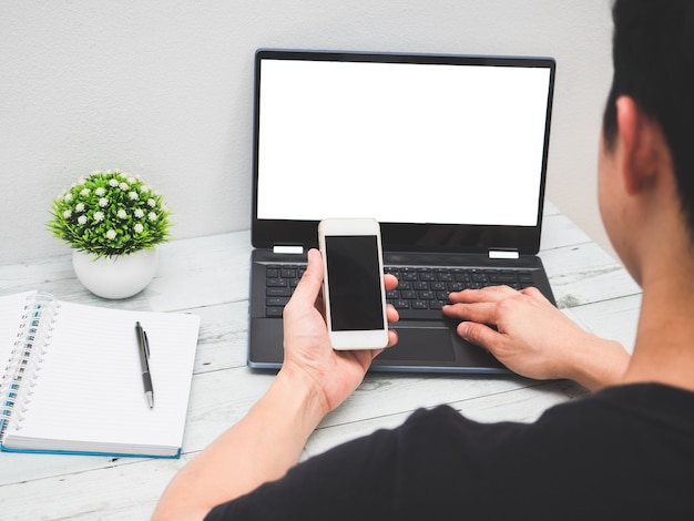 back view man holding smartphone in hand and working with laptop on the desk work space