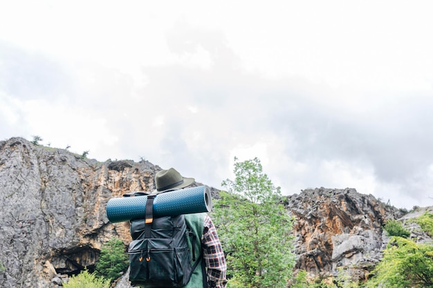 Back view of a man with backpack and hat hiking in the mountains at sunset Travel and active lifestyle concept