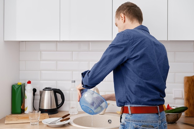 Back view of a middle aged man washes the dishes after cooking at home