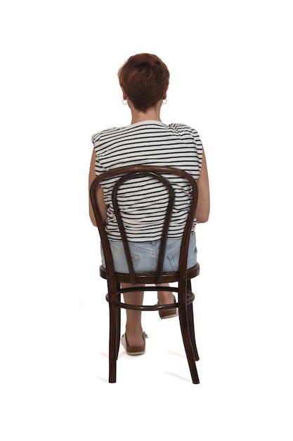 Back view of middle aged woman sitting legs on chair legs crossed on white background