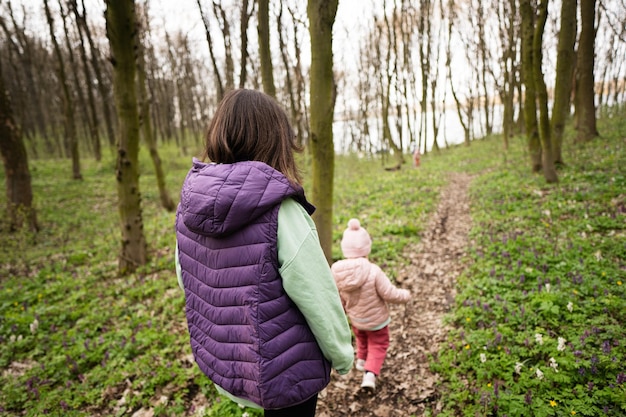 Back view of mother with daughter walking on forest trail Outdoor spring leisure concept