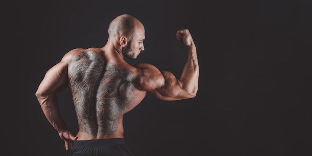 BAck view of a muscular man with tattoo on back against of black background Isolated