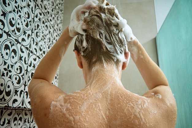 Back view of naked woman taking shower in shower stall woman washing her hairs in bathroom morning h