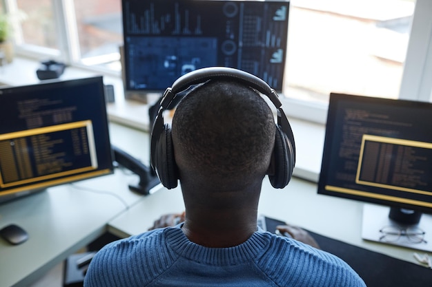 Back view portrait of software developer at workstation with multiple computer screens