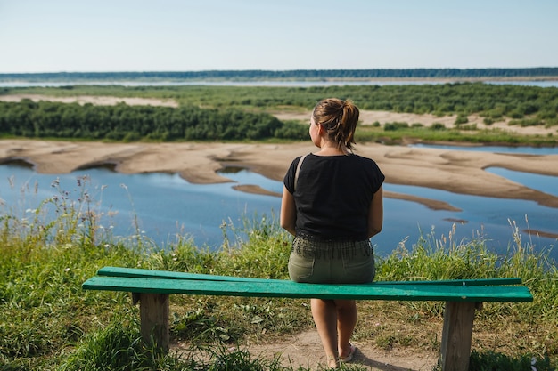 Back view pretty woman watching the amazing summer landscape in a bench