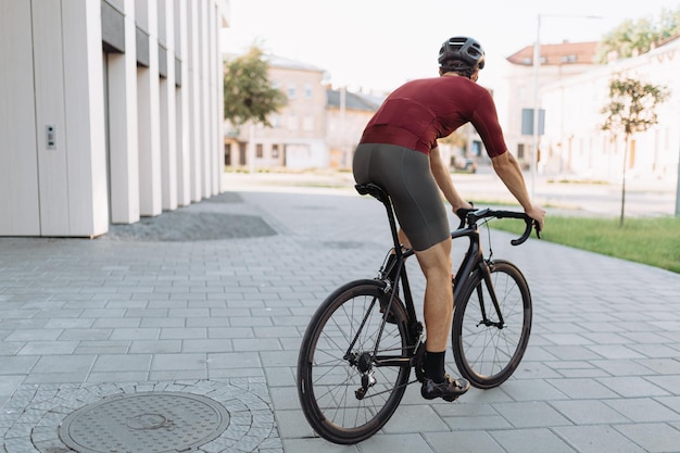 Back view of professional cyclist in sport clothes and safety helmet riding black bike during free time at urban area Concept of active and healthy lifestyles