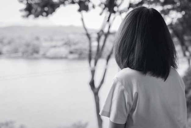 Back view of sad Asian woman in the park look the view of lake Depressed woman Mental health concept