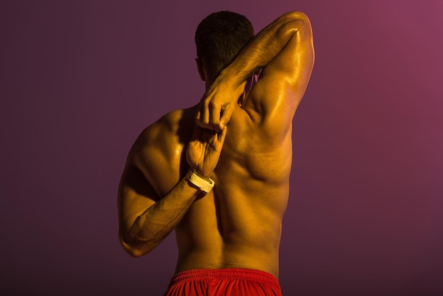 Back view of sportive man with muscular torso stretching on purple background