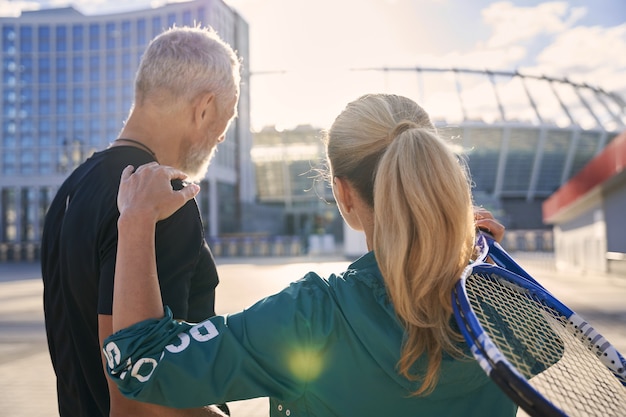 Back view of sportive middle aged couple tennis players with tennis racket standing together