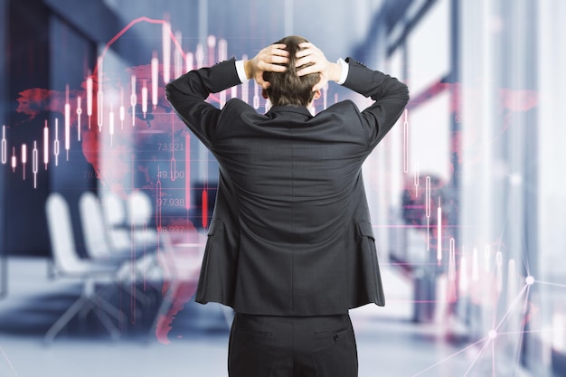 Back view of stressed businessman with glowing falling red forex chart on blurry office interior background Stock exchange and crisis concept Double exposure