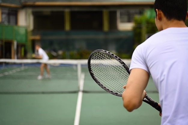 Back view of tennis player standing in ready position to receive a serve practicing for competition on a court