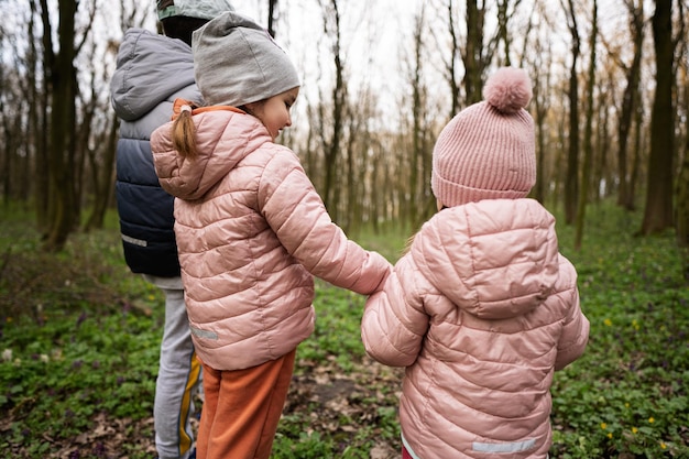 Back view of three kids holding hands walking on forest trail Outdoor spring leisure concept