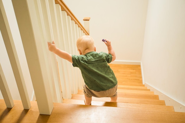 Back view toddler boy going down the wooden stairs Little boy using stairs by himself for the first time Growing up brave and confident boy