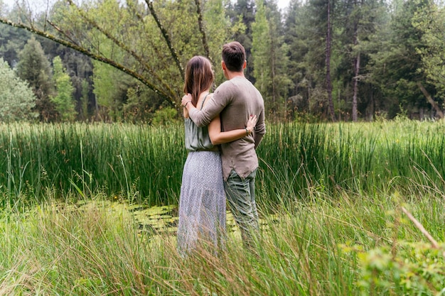 Back view of unrecognizable couple in love hugging in the forest. Horizontal view of couple hugging with love outdoors in nature background. People and travel concept.