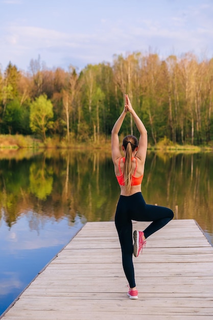 Back view of woman doing Vrksasana exercise on one leg hands up