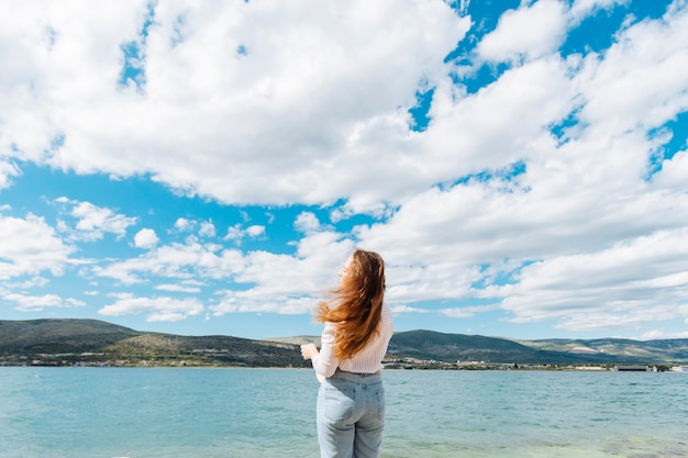 Back view of woman enjoying the view of the ocean with mountains