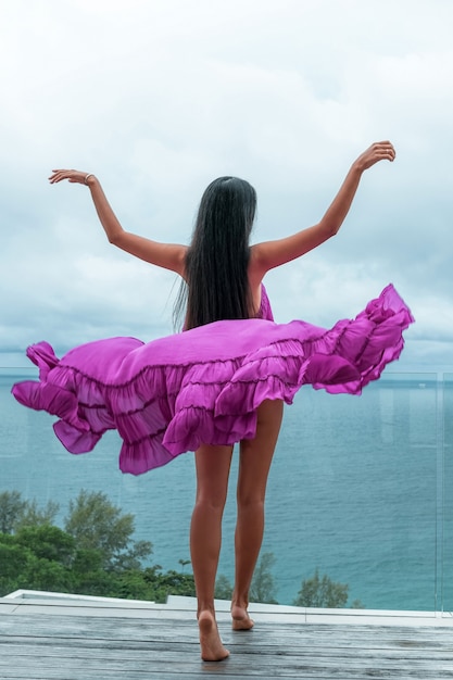 Back view: a woman in a long openwork purple cape poses on a transparent terrace