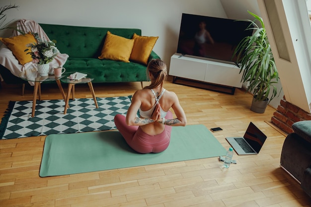 Back view of woman seated on a yoga mat in a living room with hardwood flooring