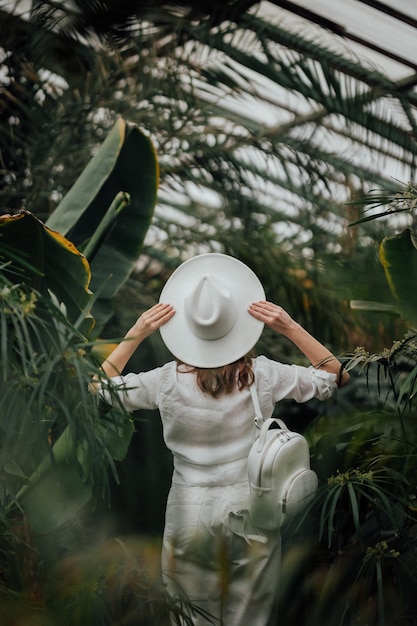 Back view of woman tourist in a hat standing in palm greenhouse of botanical garden