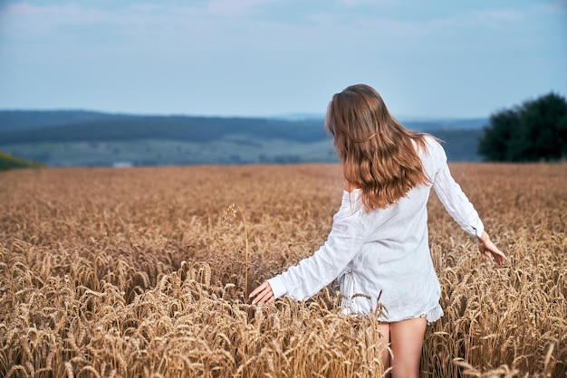 Back view of woman in white dress standing on wheat field