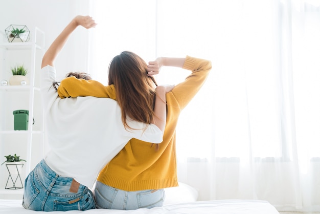 Back view of women lesbian happy couple waking up in morning, sitting on bed