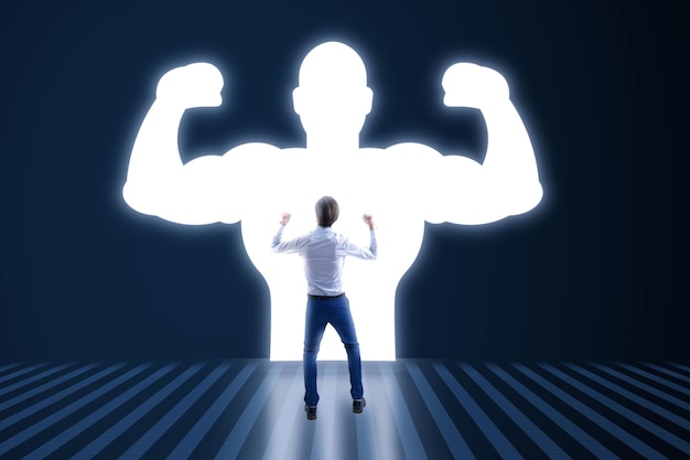 Back view of young businessman with very strong illuminated shadow flexing muscles on dark wall background Personal development inner strength motivation concept