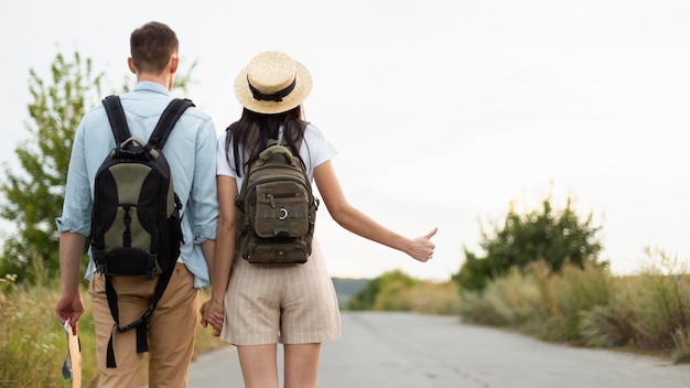 Back view young couple hitch hiking