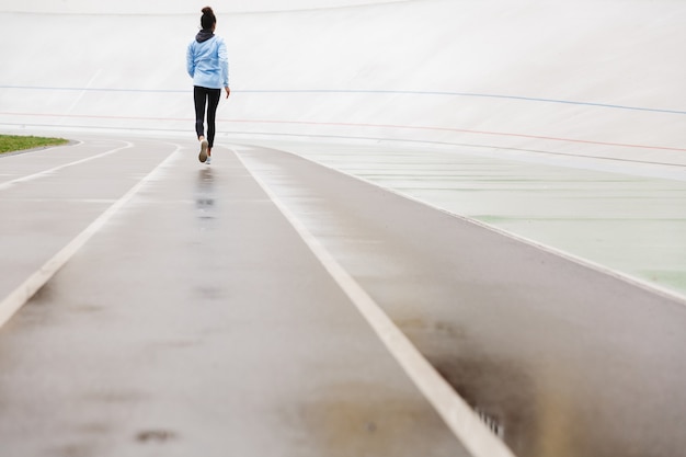 Back view of a young fit african sportswoman running at the stadium