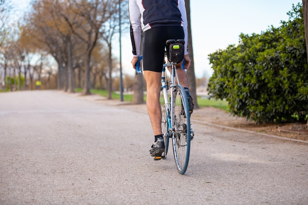 Back view of young male cyclist in sportswear and protective helmet cycling bike on road in park