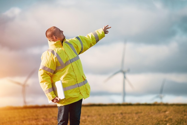 Back view of young male engineer in a wind turbine farm in the background