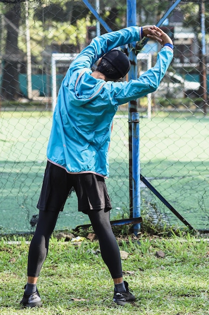 Back view of young man stretching before workout at public fitness facility outdoor, working on arms