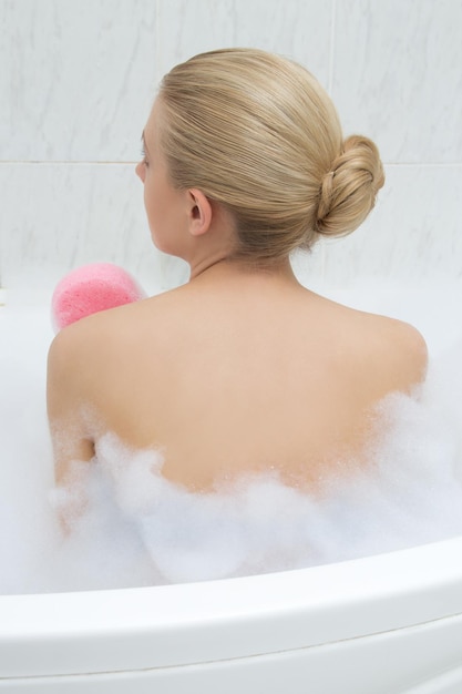 Back view of young sexy woman relaxing in bath and washing herself