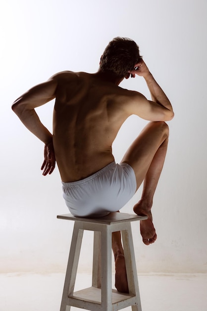 Back view of young shirtless muscled man wearing white boxers standing isolated on gray background