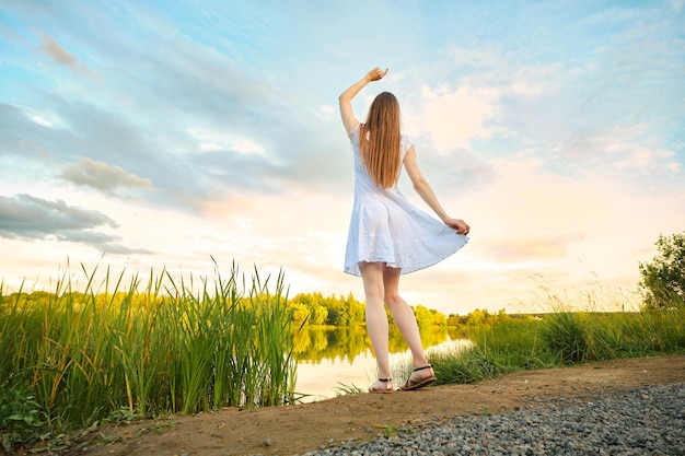 Back view of young woman enjoying sunset standing by the river bank