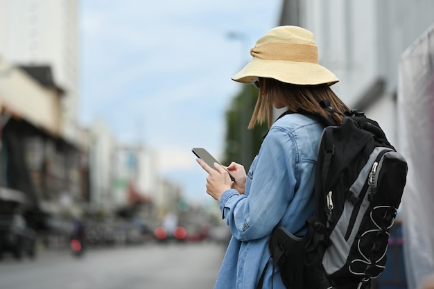 Back view of young woman traveller using smartphone platform applications for helping tourism about travel map GPS