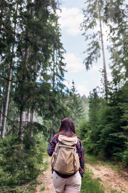 Back view young woman walks with backpacker in the forest Travel and summer vacations outdoor lifestyle concept