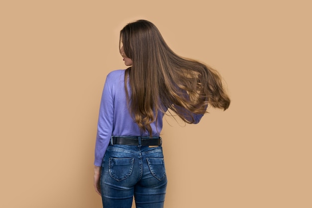 Back view Young woman with blowing long hair isolated on beige background Hairstyle Hair care