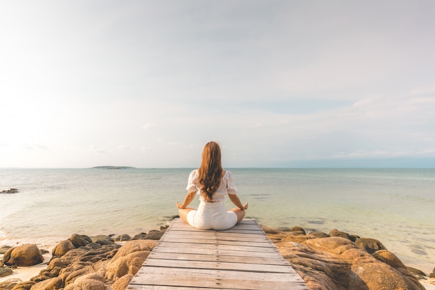 Back of views woman practice yoga lotus pose to meditation summer vacation on pier with sae and beach feeling so happiness