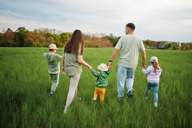 Back of walking parents with three kids having fun together at meadow